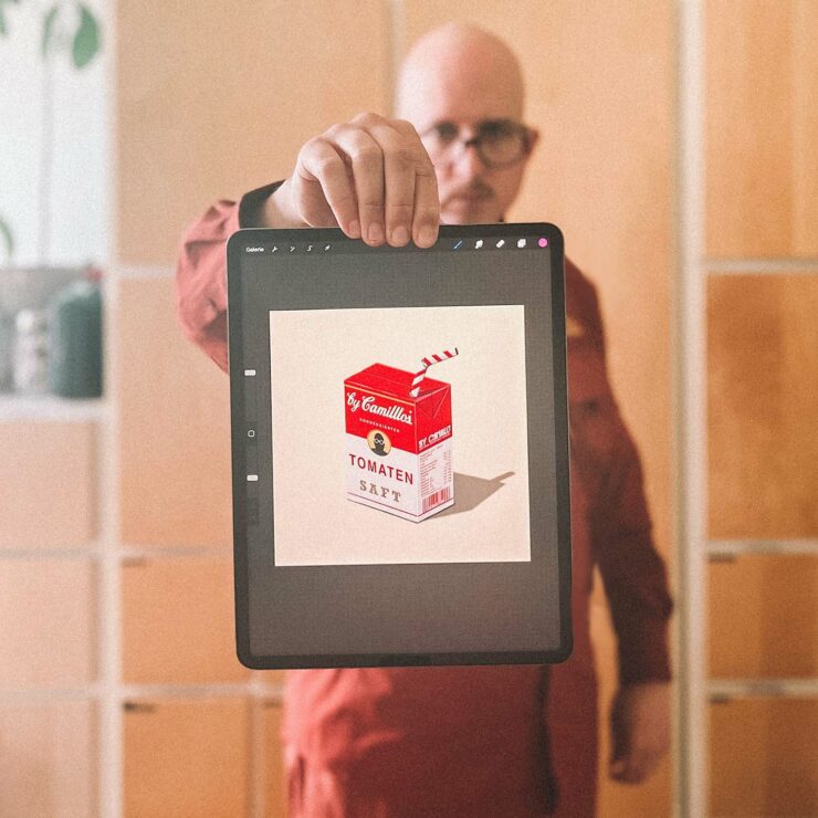 Camillo Richter hält ein Tablet, auf dem eine Illustration einer Retro-Tomatensaft-Verpackung zu sehen ist. Auf der Verpackung steht „by Camilllo – Tomatensaft“ mit einem roten Strohhalm.